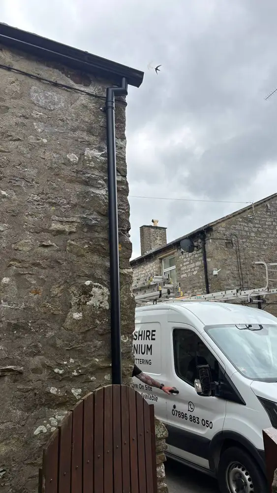 Black aluminium downpipe and guttering on a rural stone house
