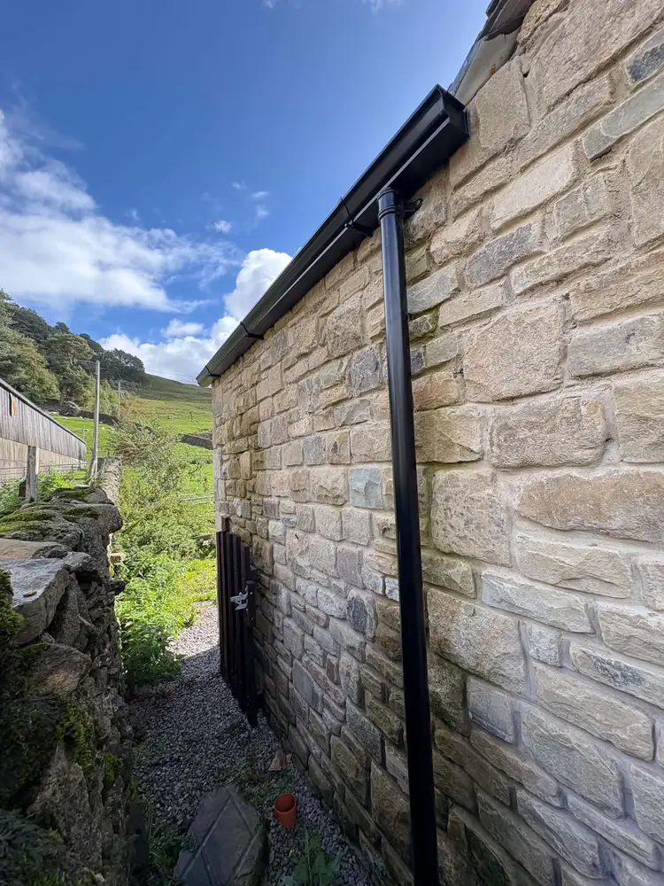 Black guttering and downpipe on a stone building beside a rural path