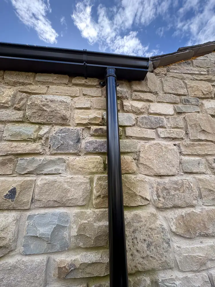 Black gutter and downpipe fitted neatly to a stone wall