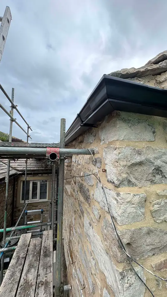 Close view of newly installed black guttering on a traditional stone roofline