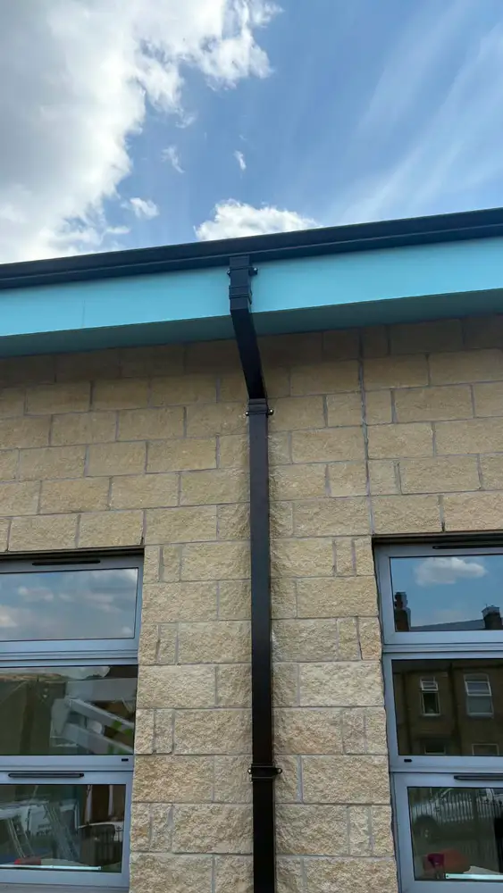 Black square downpipe and guttering fitted to a stone commercial building
