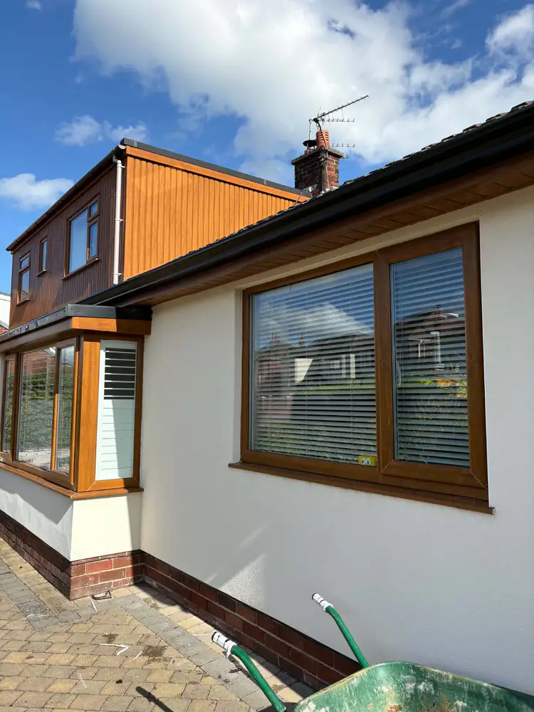 Black guttering along a white rendered extension with timber cladding