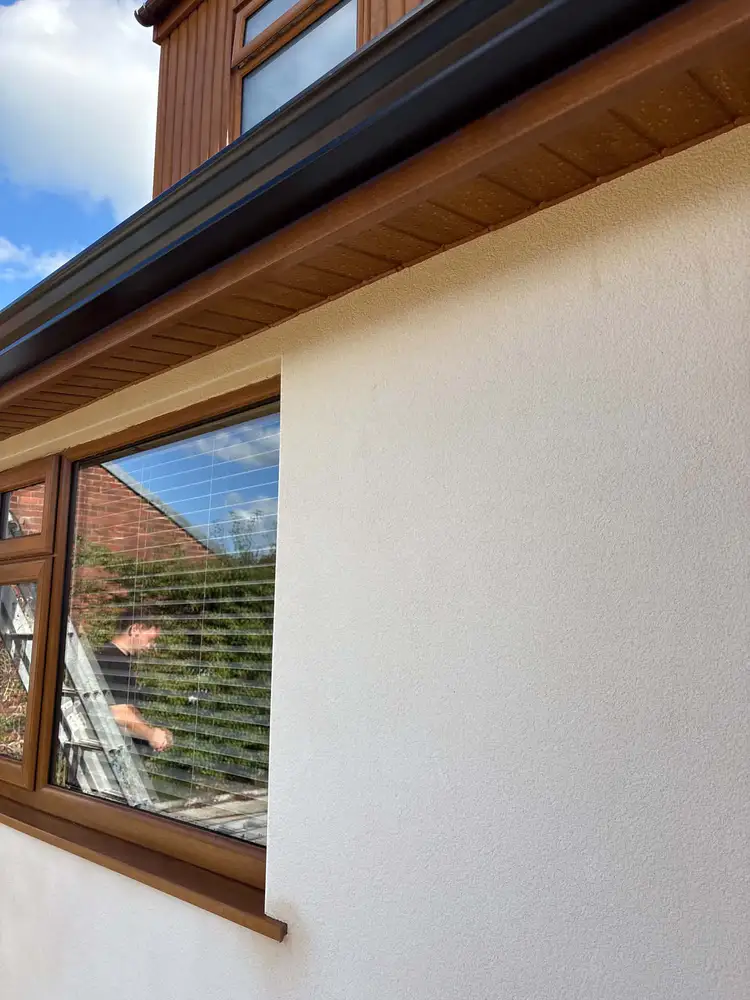 Black guttering above a timber soffit and brown framed window