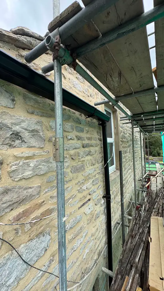 Black gutter and downpipe installation viewed from scaffolding