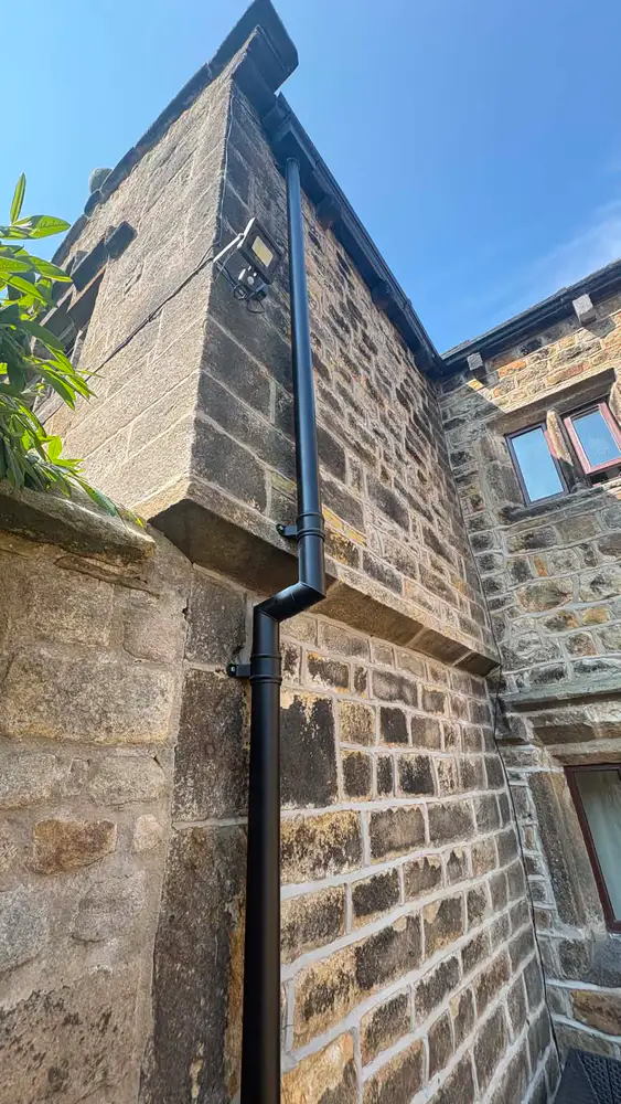 New black aluminium downpipe fitted neatly to a traditional Lancashire stone property