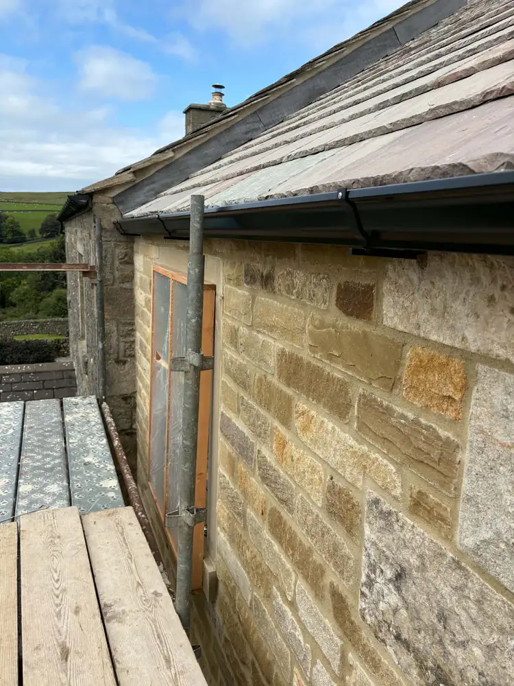 Black gutter fitted below a slate roof with scaffold access alongside