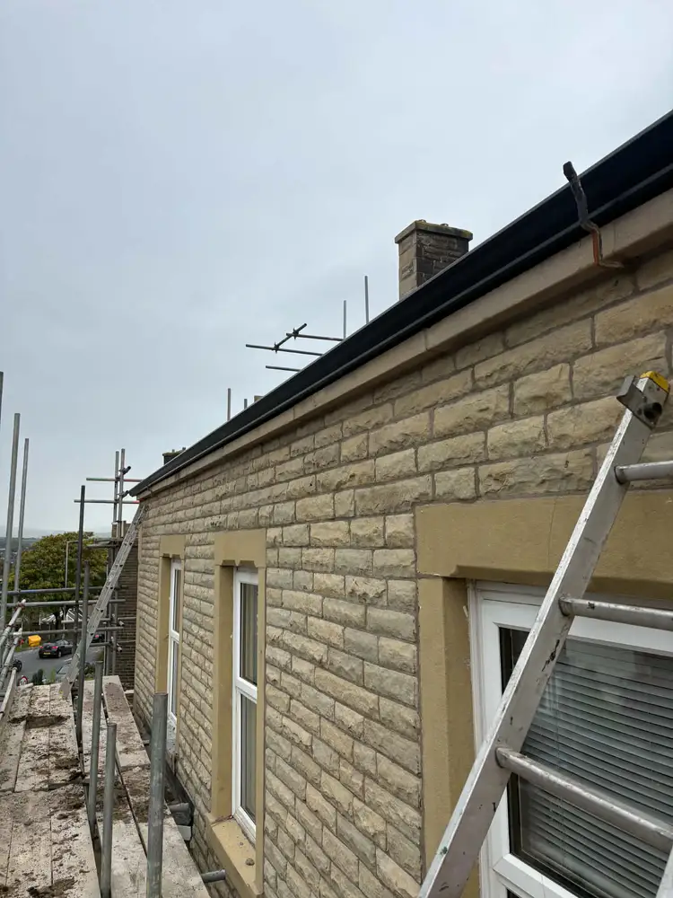 Guttering installation along a stone house with scaffolding and a ladder