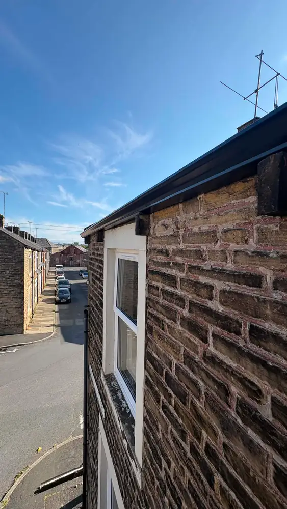 Black seamless guttering fitted to a traditional stone terrace under a blue sky